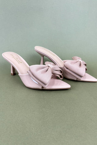 Pair of light pink high-heeled shoes with large bows on a green background