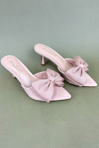 Pair of light pink high-heeled shoes with bow details on a green background