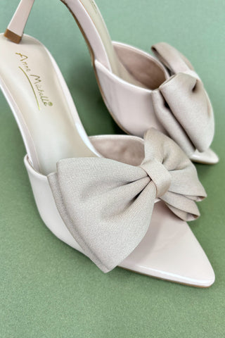White high-heeled shoes with large bows on a green background