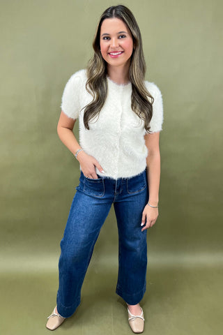 Woman wearing a white knitted vest and blue jeans against a green background