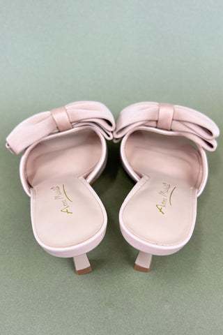 Pair of pink high-heeled shoes with bow details on a light green background