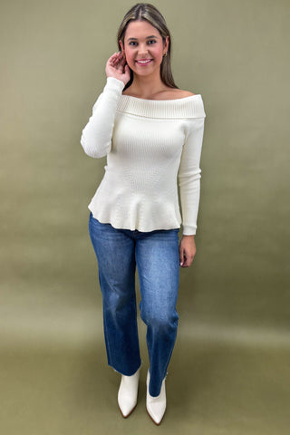 Woman wearing a white off-shoulder top and blue jeans on a green background