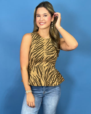 A woman modeling a sleeveless peplum top with a tan and brown zebra print, paired with blue jeans