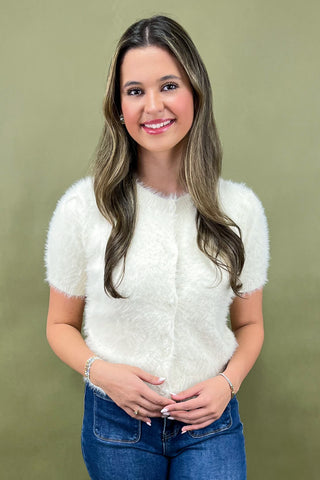 Woman wearing a white fluffy top and blue jeans against a green background