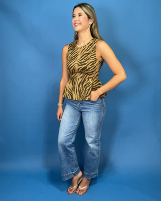 A woman modeling a sleeveless top with a tan and black zebra print, paired with blue jeans