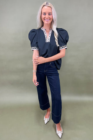 Woman wearing a navy top with white trim and dark jeans against a plain background