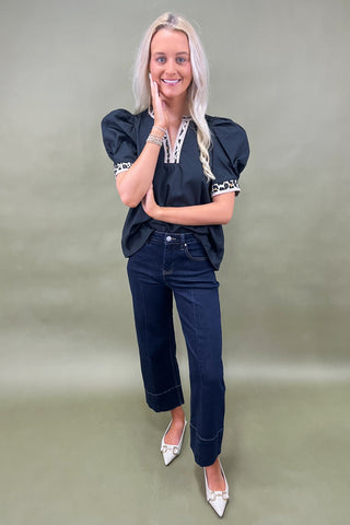 Woman wearing a black top with white accents and dark jeans on a plain background