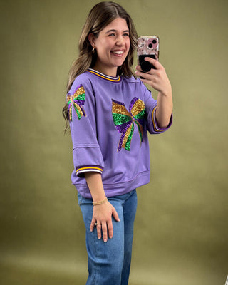 Woman taking a selfie wearing a purple sweatshirt with colorful designs on a green background