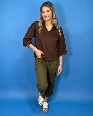 Chocolate brown collared top with a V-neckline, three-quarter sleeves, and scalloped trim along the cuffs and hem.