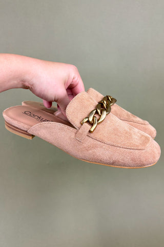 Beige loafers with gold chain detail held by a hand against a neutral background