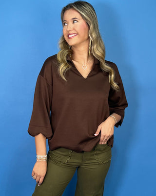 Chocolate brown collared top with a V-neckline, three-quarter sleeves, and scalloped trim along the cuffs and hem.