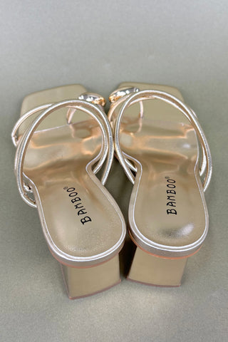 Pair of gold sandals with clear straps on a gray background, featuring the brand 'Bamboo'.