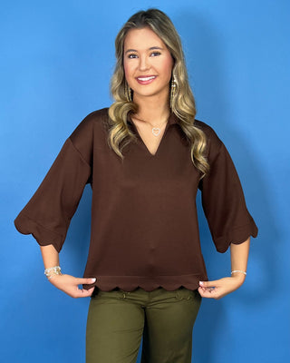 Chocolate brown collared top with a V-neckline, three-quarter sleeves, and scalloped trim along the cuffs and hem.