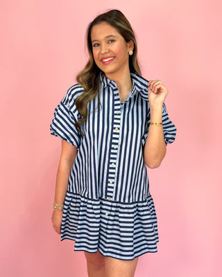 Woman wearing a navy and white striped dress against a pink background