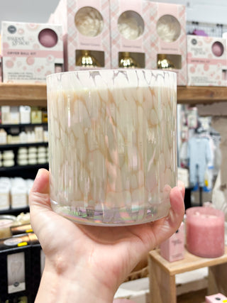 Hand holding a marbled candle in a store setting with various products in the background.