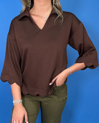 Chocolate brown collared top with a V-neckline, three-quarter sleeves, and scalloped trim along the cuffs and hem.