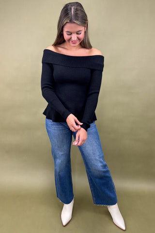 Woman wearing a black off-shoulder top and blue jeans on a beige background