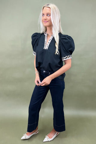 Woman wearing a black top with white accents and dark jeans on a plain background