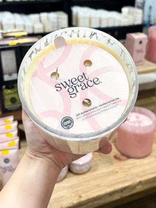 Hand holding a 'sweet grace' candle in a store setting