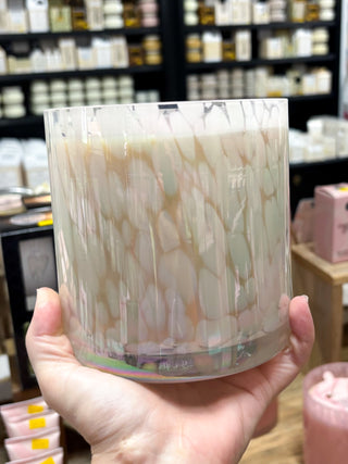 Marbled glass candle held in a hand with a store shelf in the background
