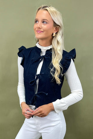 Woman wearing a navy blue vest with ruffled details on a green background