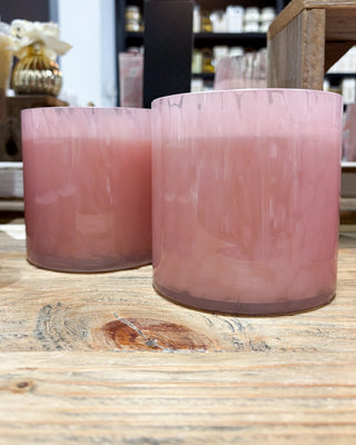 Two pink glass candles on a wooden surface with a blurred background