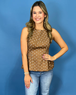 A woman modeling a brown sleeveless top with white polka dots, paired with light blue jeans