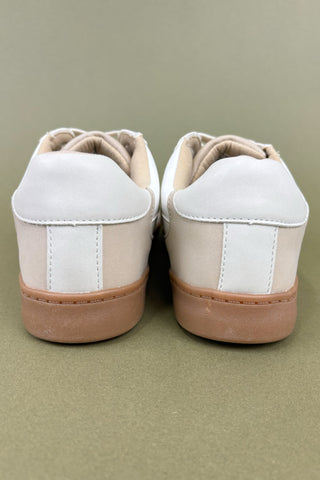 Pair of beige sneakers with white soles on a green background