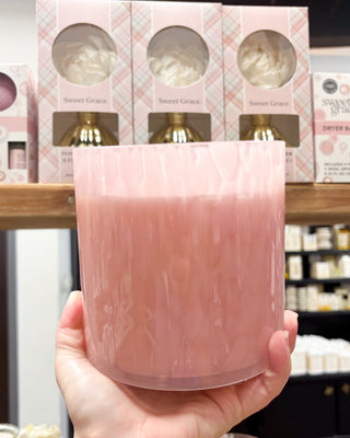 Hand holding a pink candle with product packaging in the background
