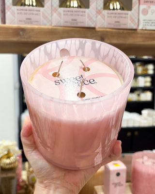 Pink candle labeled 'sweet spice' held by a hand with blurred store shelves in the background