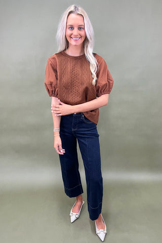 Woman wearing a brown top and blue jeans against a plain background