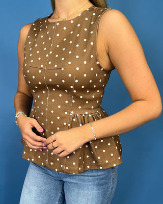 A woman wearing a sleeveless brown top with white polka dots and a peplum waist, paired with blue jeans