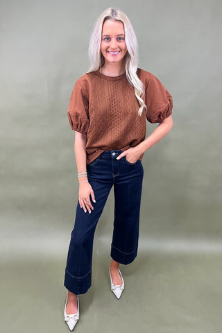 Woman wearing a brown top and blue jeans against a plain background