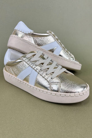 Pair of silver sneakers with white soles on a green background