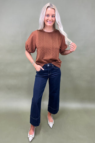 Woman wearing a brown top and blue jeans against a plain background