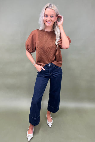 Woman wearing a brown top and blue jeans against a plain background
