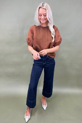 Woman wearing a brown top and blue jeans against a plain background
