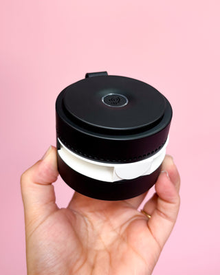 Hand holding a black and white container against a pink background