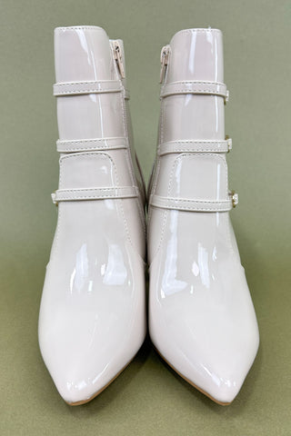 Pair of white patent leather pointed-toe boots with strap details on a green background