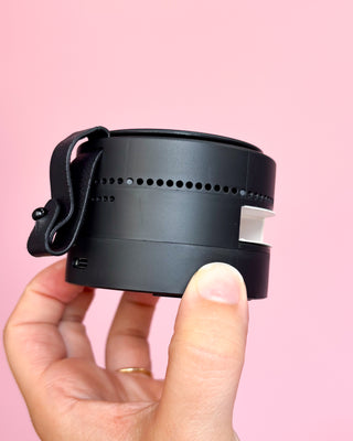 Black camera lens with white accents held by a hand against a pink background
