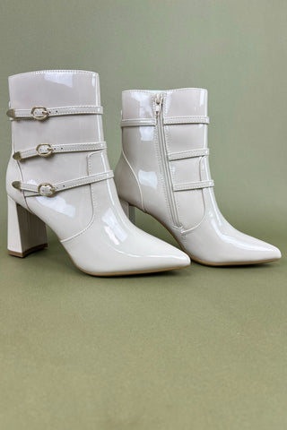 White patent leather boots with multiple straps on a green background