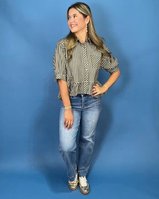 A woman modeling a black and white gingham check blouse with puff sleeves and a ruffled hem, paired with blue jeans and sneakers
