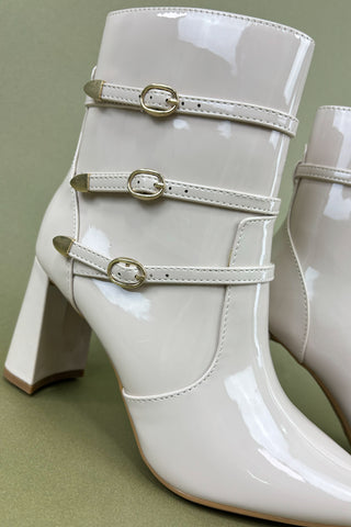 White patent leather boots with gold buckles on a green background