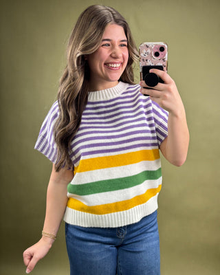 Woman wearing a colorful striped sweater taking a selfie against a green background