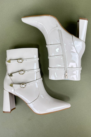 White patent leather boots with buckles on a green background