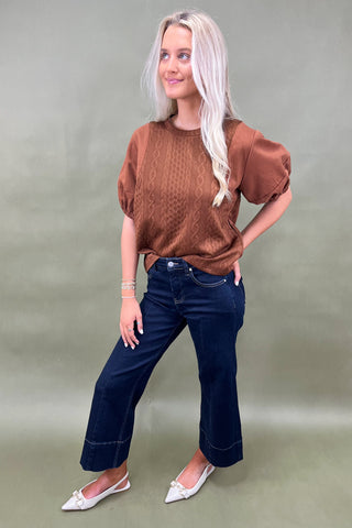 Woman wearing a brown top and blue jeans against a plain background