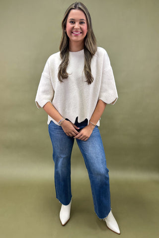 Woman wearing a white sweater, blue jeans, and white shoes on a green background