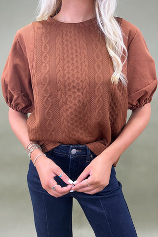 Woman wearing a brown top and blue jeans against a plain background
