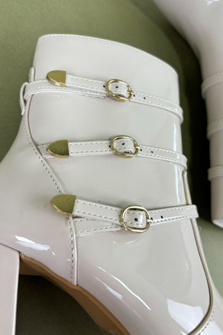 White high-heeled shoes with gold buckles on a green background