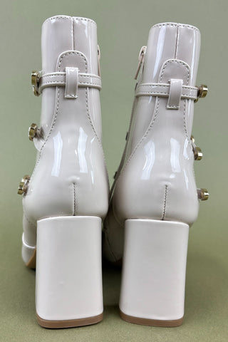 White patent leather boots with gold buckles on a green background